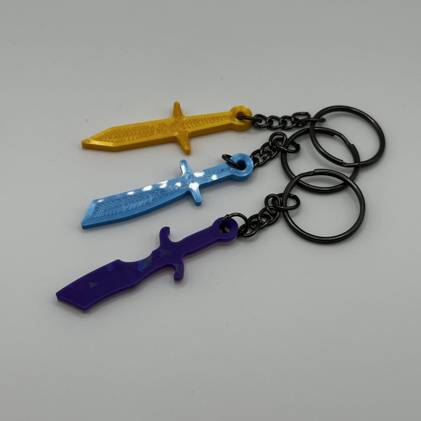 Three mini throwing knife keychains in gold, blue and purple