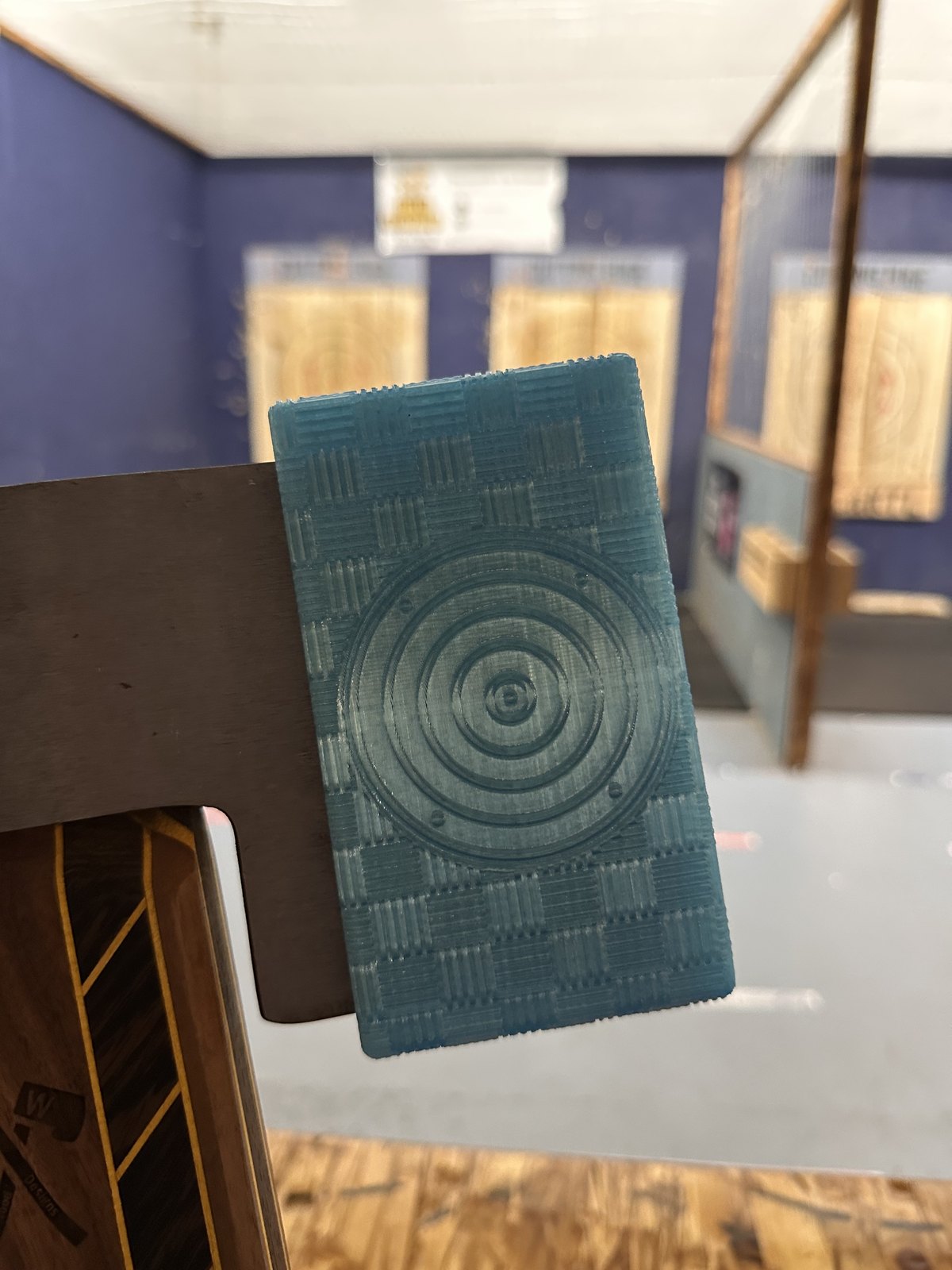 Teal crosshatch sheath fitted on a hatchet at an axe throwing venue, lanes and targets behind